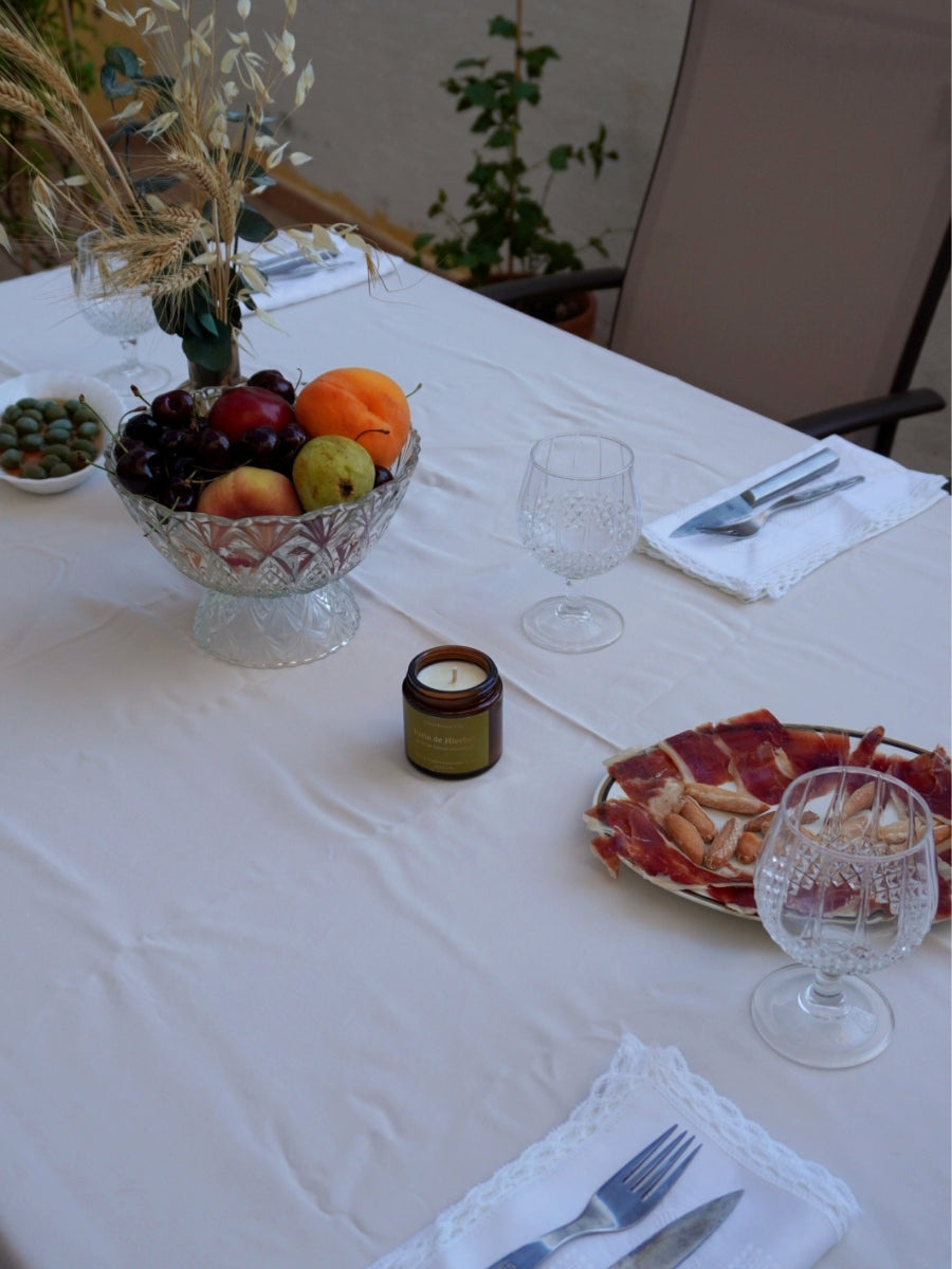 Vela Patio de Hierbas de Naturaleza en Vela en mesa de cena al aire libre con mantel blanco y decoración de jardín.  Vela artesanal de cera de soja con aceites esenciales repelentes
